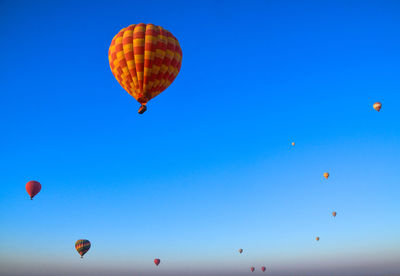 Low angle view of hot air balloons flying against clear blue sky