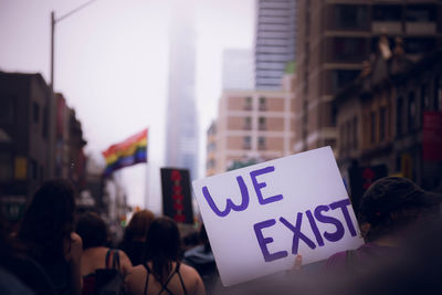 Rear view of woman holding banner with message amidst crowd during protest