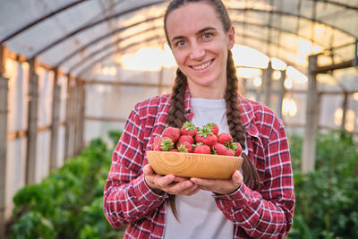 Happy female harvested fresh organic strawberry greenhouse wood plate in front