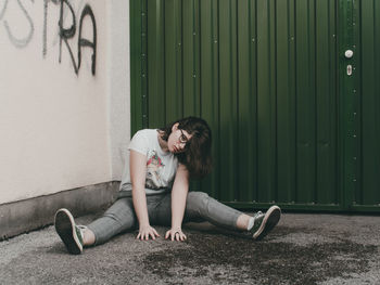 Full length of young woman sitting against wall