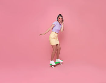 Full length portrait of woman standing against pink background