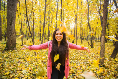 Smiling young woman standing in forest during autumn