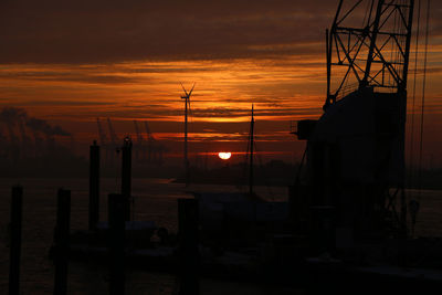 Silhouette electricity pylon by sea against orange sky