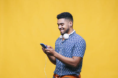 Young man using mobile phone against yellow background