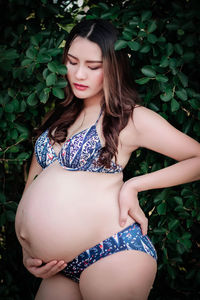 Pregnant woman touching belly while standing against plants