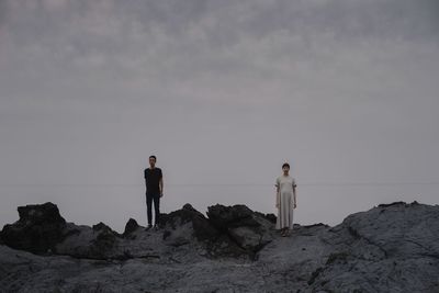 Rear view of woman walking on rock at beach against sky