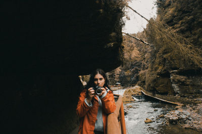 Young woman standing against rock wall and river