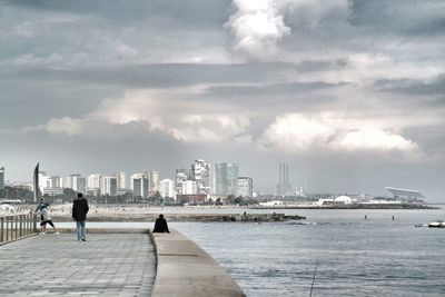 People walking in city against cloudy sky