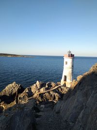 Lighthouse by sea against clear sky