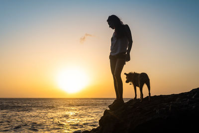 Full length of woman with dog on beach against sky during sunset