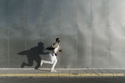 Man running on footpath by metallic wall