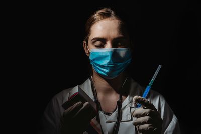 Portrait of young woman wearing mask against black background