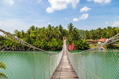 Footbridge amidst plants and trees against sky