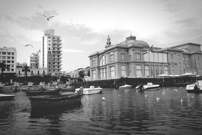 Boats moored at harbor against sky in city