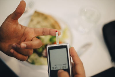 Businessman using glaucometer in blood test while having food at table