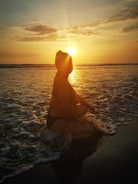 Man sitting on beach against sky during sunset