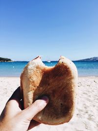 Close-up of hand holding ice cream at beach against clear blue sky