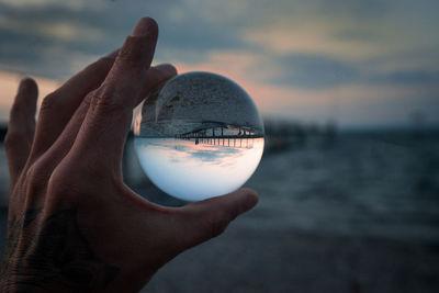 Close-up of hand holding crystal ball against sky during sunset