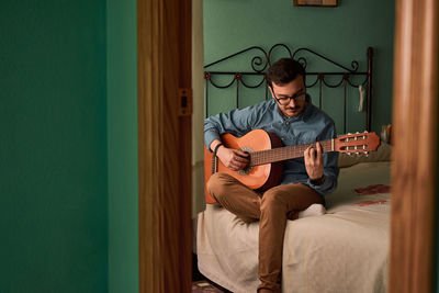 Young man plays guitar in a room in his house