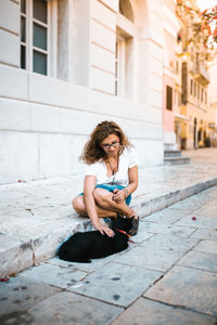 Woman stroking cat on footpath in city