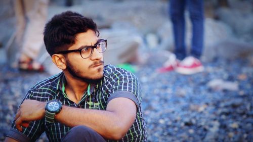 Young man looking away while sitting outdoors