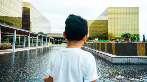 Rear view of man standing in swimming pool against buildings