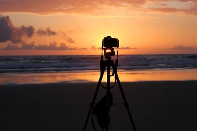 Man photographing on beach against sky during sunset