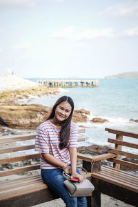 Portrait of smiling young woman sitting against sky