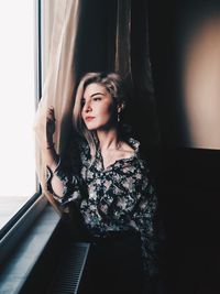 Young woman looking through window standing at home