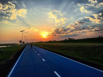 Rear view of people riding bicycles on road against sky during sunset