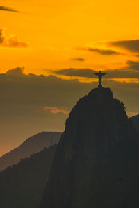 Silhouette sculpture on rock against sky during sunset