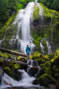 Young woman looking up at huge waterfall in forest