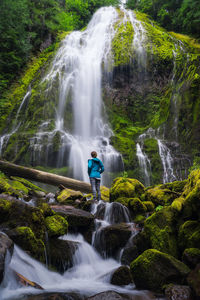 Young woman looking up at huge waterfall in forest