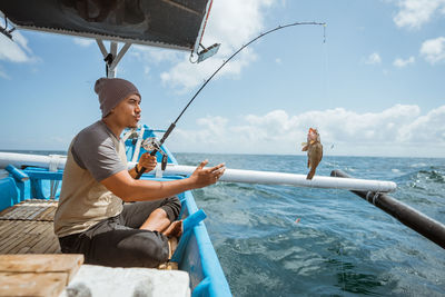 Side view of man using mobile phone at sea against sky