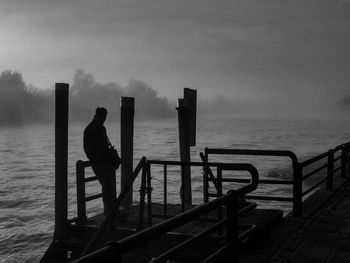 Silhouette man standing on pier over lake against sky