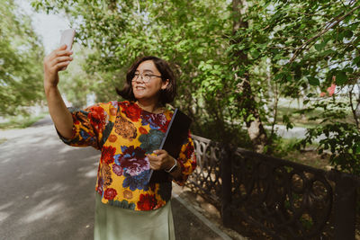 Happy adult woman taking a selfie with her mobile phone in blooming park.