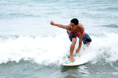 Full length of shirtless man surfing in sea