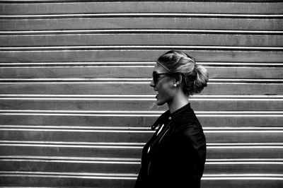 Side view of young woman standing against shutter