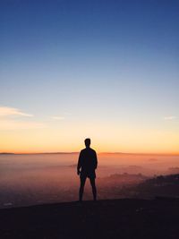 Rear view of silhouette man standing on mountain against sky