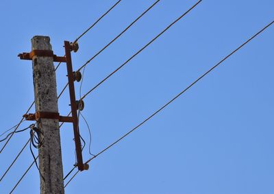 Low angle view of electricity pylon against clear blue sky