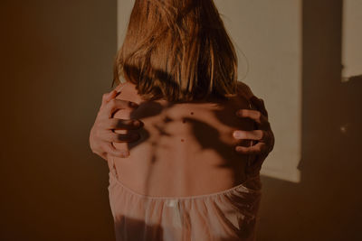 Rear view of woman standing against wall at home