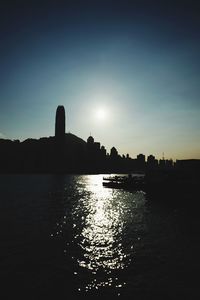 Scenic view of river by silhouette city against sky during sunset