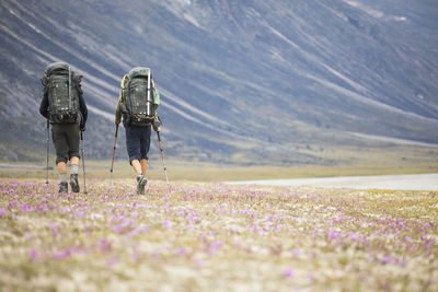 Rear view of women walking on landscape against cloudy sky