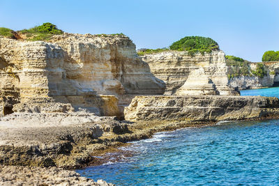 Rock formations by sea against clear blue sky