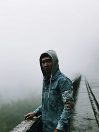 Portrait of man standing by retaining wall during foggy weather