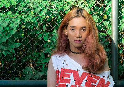 Portrait of young woman with long hair standing against fence