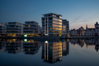 Reflection of buildings in lake against sky at dusk