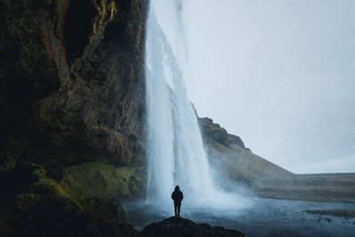 Rear view of person standing on rock by waterfall