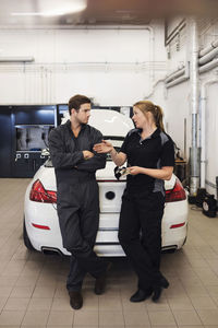 Full length of mechanics discussing while standing against car in shop