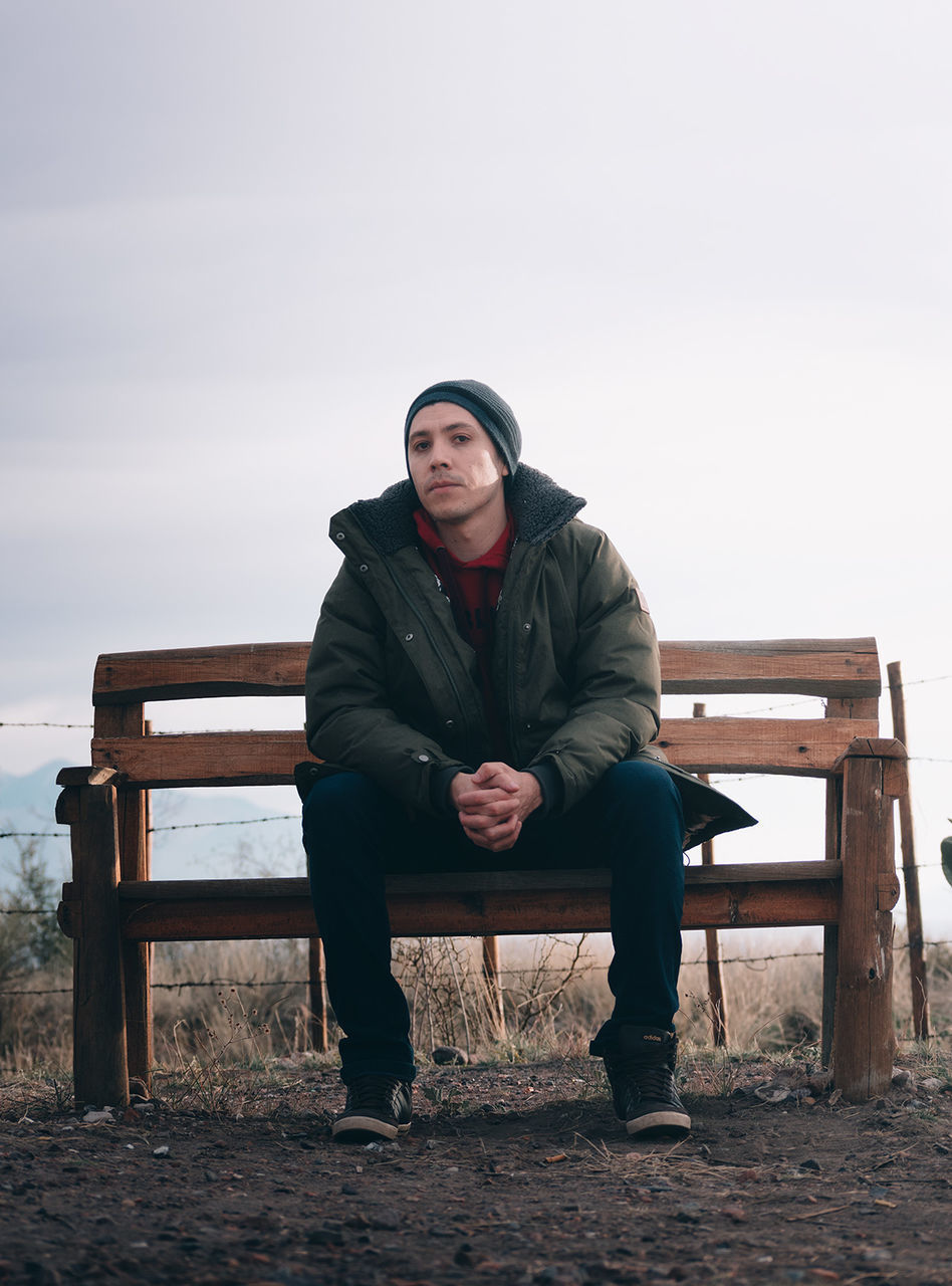 PORTRAIT OF YOUNG MAN SITTING ON BENCH